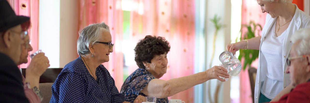 DRK-Mitarbeiterin schenkt Seniorinnen und Senioren frisches Wasser ein.